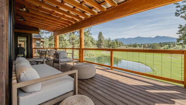Une terrasse en bois avec un canapé, des fauteuils et un pouf, offrant une vue sur un terrain de golf et des montagnes.
