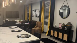 Ein modernes Wohnzimmer mit Essbereich, einer Couch, einem Couchtisch und einem an der Wand montierten Fernseher.