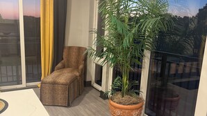 Ein modernes Wohnzimmer mit großem Fenster, einem leopardenmusterigen Sessel, einer Topfpflanze und einem Tisch mit Marmorplatte.