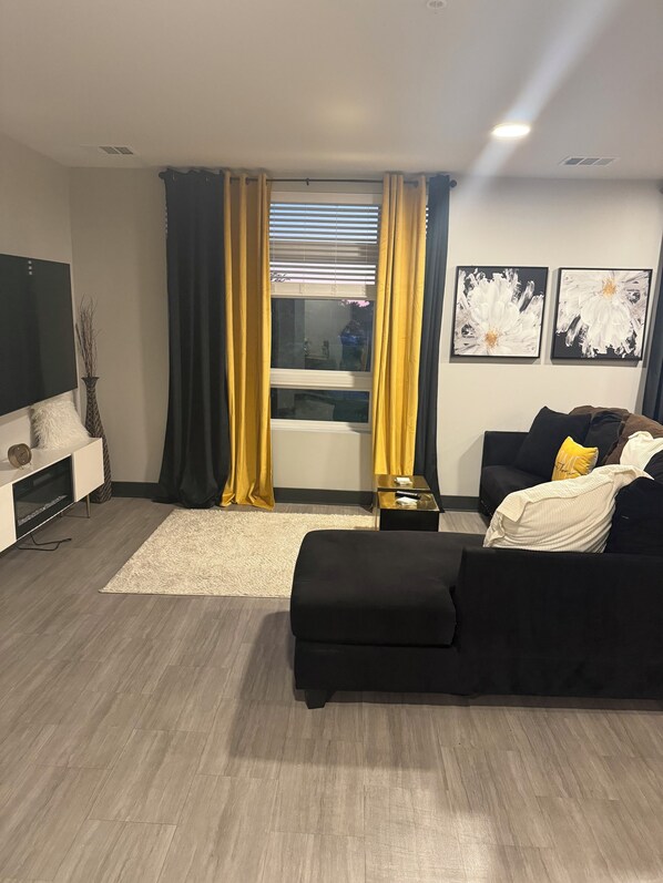 A modern living room with a black sofa, a white rug, and a TV on a stand.