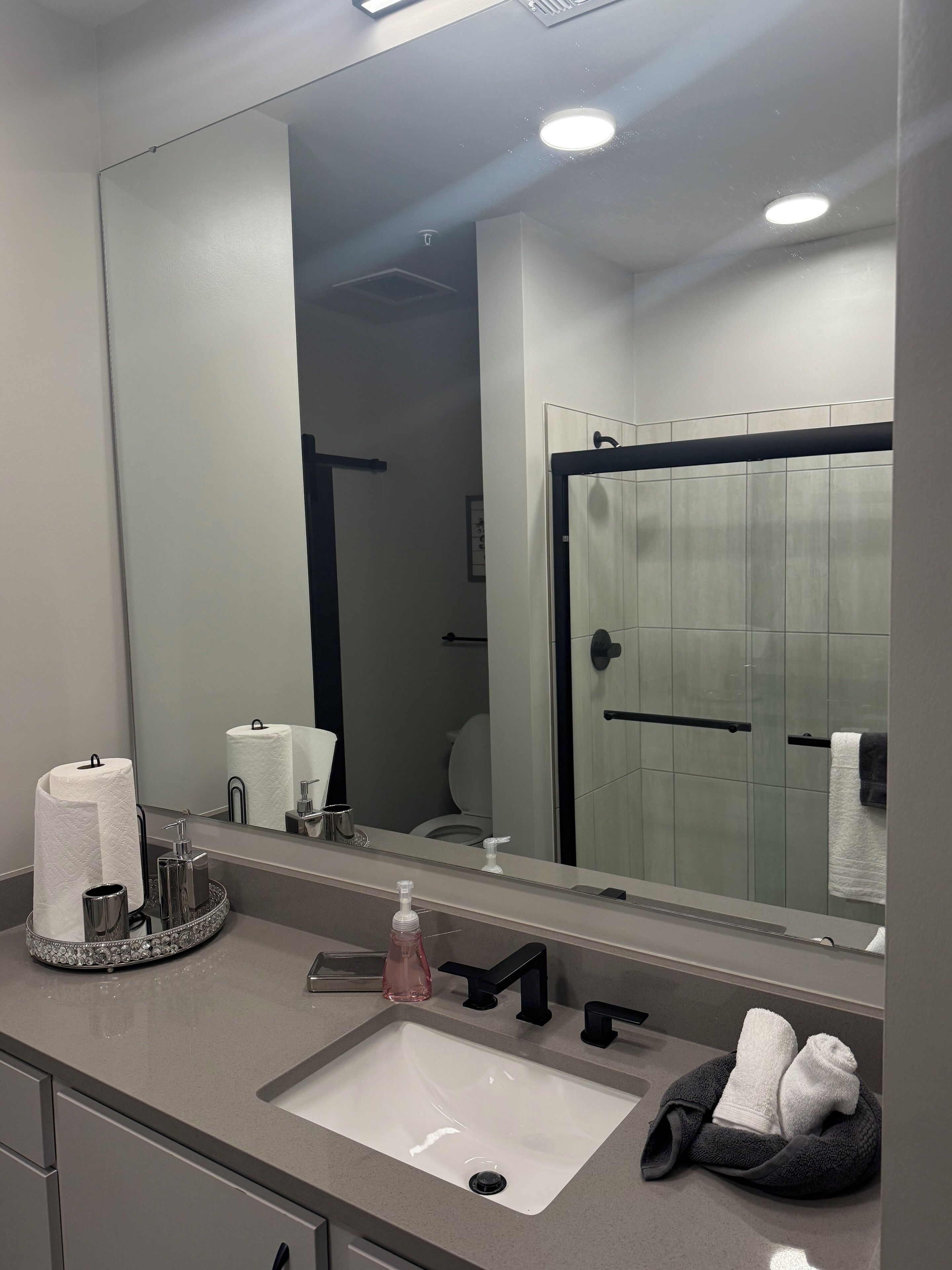 Ein modernes Badezimmer mit großem Spiegel, Waschbecken und Duschbereich.