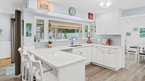 Una cocina moderna con muebles blancos, una isla central y un comedor con sillas blancas.