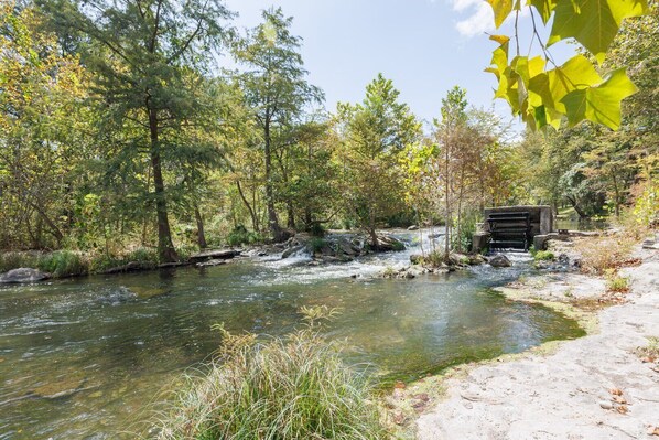 A river flowing through a forested area with a small bridge and a bench.