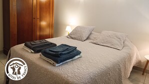 Ett sovrum med en säng, två kuddar, en trägarderob och hopvikta handdukar.