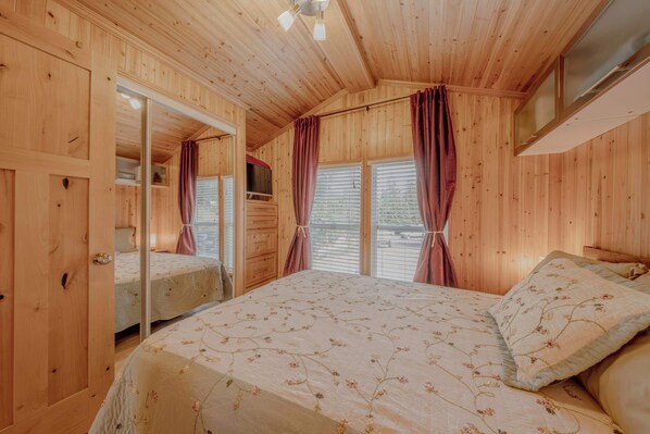 A wooden-paneled bedroom with a bed, a mirror, and a window with curtains.