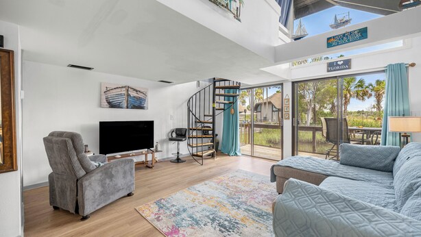 A spacious living room with a large TV, comfortable seating, a spiral staircase, and a view of the outdoors. - Bring Your Boat-Waterfront Bungalow- On River Time! (Crystal River)