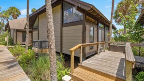 A modern two-story building with large windows, a wooden deck, and surrounding palm trees. - Bring Your Boat-Waterfront Bungalow- On River Time! (Crystal River)