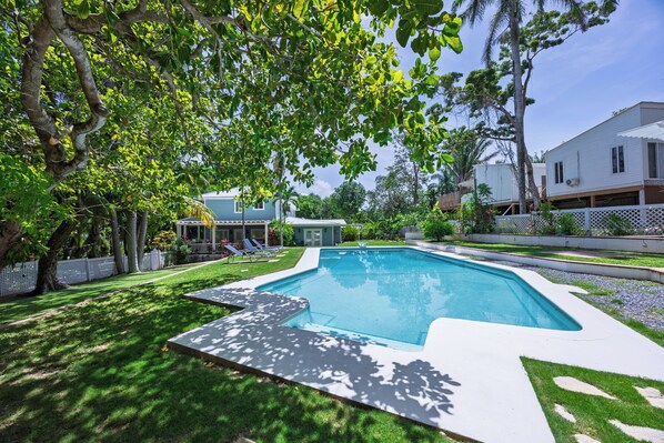 A swimming pool with a surrounding deck, a lawn, and a house in the background.