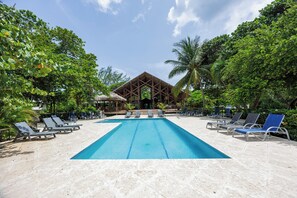 A swimming pool with lounge chairs and a building with a thatched roof.