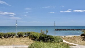 Un sendero costero con vistas despejadas al mar, un rompeolas rocoso y vegetación escasa.