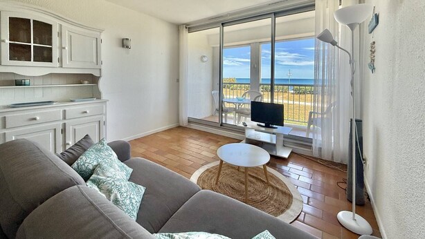 Una sala de estar con sofá, televisión y balcón con vista a la playa.