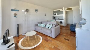 Un espacio habitable compacto con sofá, una mesita redonda, televisor, lavadora y kitchenette.