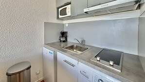 Cocina compacta con microondas, cafetera, fregadero, lavavajillas y cubo de basura.