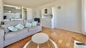 Una sala de estar con sofá, una mesa redonda de centro, una zona de cocina con armarios y microondas, y un comedor con mesa y sillas.