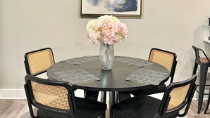 A round dining table with black chairs, a vase with flowers, and a framed abstract painting on the wall.