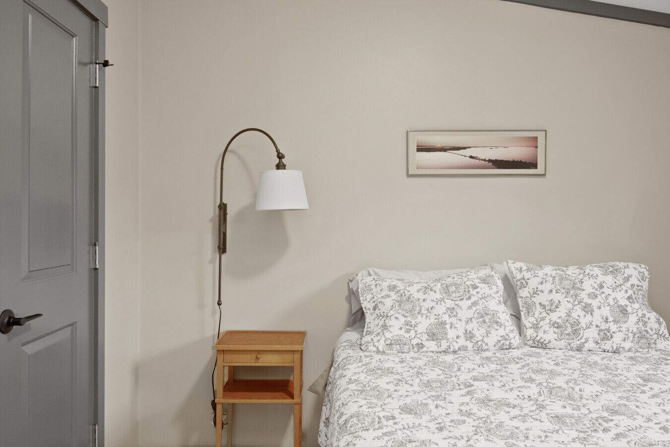 Un dormitorio con cama, mesita de noche, lámpara y un cuadro en la pared.