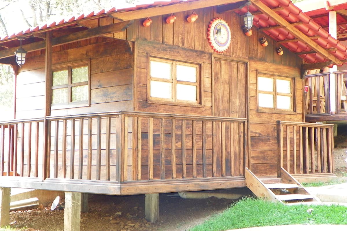 A wooden cabin with a balcony, large windows, and a red roof.