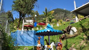 A carousel with animal figures, a blue canopy, and a grassy area with trees and a hill in the background. - OTRO ROLLO EN JILOTPEC ZACAPOAXTLA  (Zacapoaxtla)