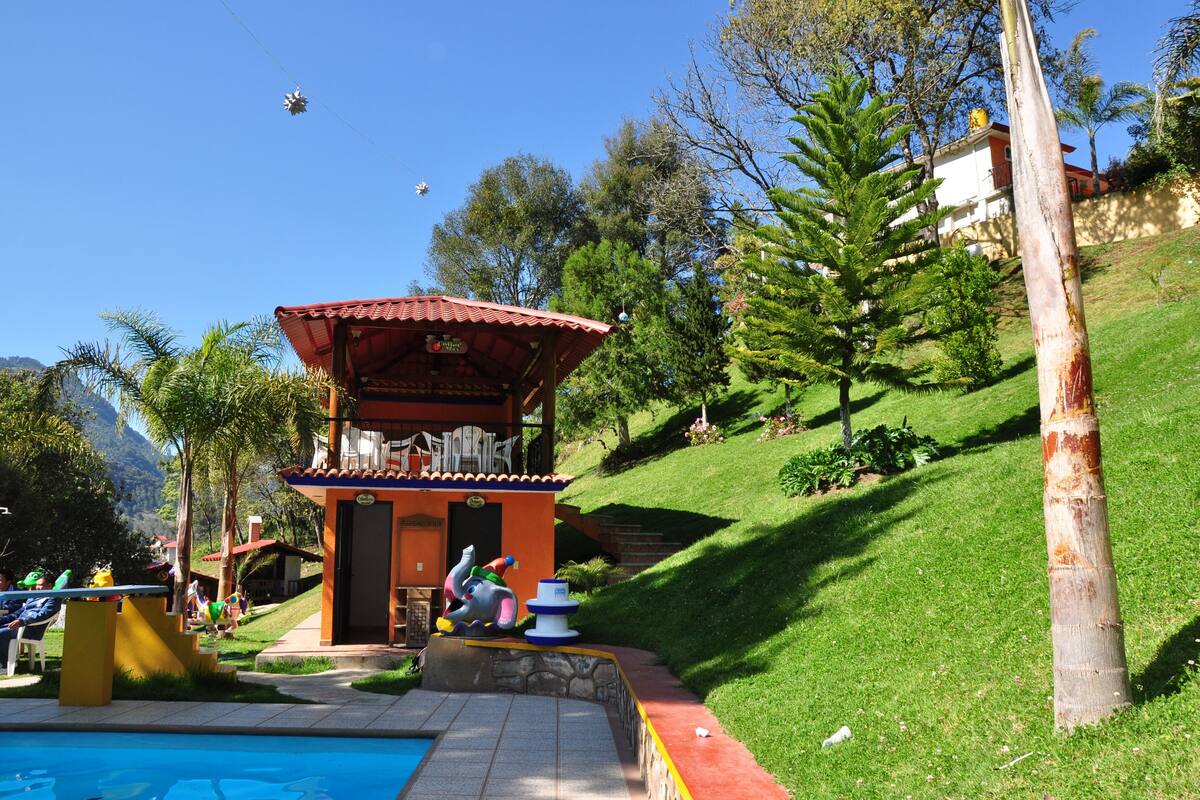 A small building with a red roof and a sign, located next to a swimming pool with a statue of a person and a blue and white structure.