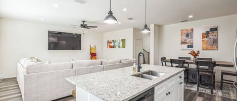 Une cuisine moderne dotée d’un plan de travail en granit, de meubles blancs et d’un coin repas avec une table et des chaises.