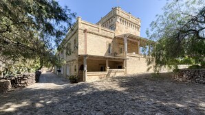 Ein Gebäude aus Stein mit einem Balkon, einem Kiesweg und Bäumen.