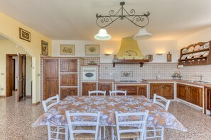 A kitchen with a dining table, chairs, wooden cabinets, a tiled backsplash, and a chandelier.