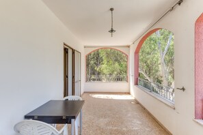 A corridor with a table and chairs, a ceiling light, and a view of trees through an arched window.