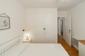Un dormitorio con cama, mesita de noche con lámpara, un cuadro en la pared y un armario blanco.