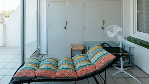 A sun lounger with colorful cushions, a small table with a woven stool, and a standing fan. - WELCS APARTAMENTO 260 EMP con vistas al canal (Empuriabrava)