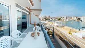 A balcony with white chairs, a table, and a vase. The balcony overlooks a marina with boats and buildings in the background. - WELCS APARTAMENTO 260 EMP con vistas al canal (Empuriabrava)