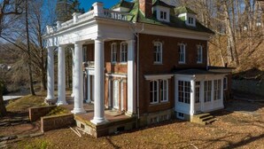 A large, historic brick house with a wrap-around porch supported by white columns, a central chimney, and a covered front porch. - Spacious 6-bedroom house with AC, WiFi in charming Springfield (Springfield)