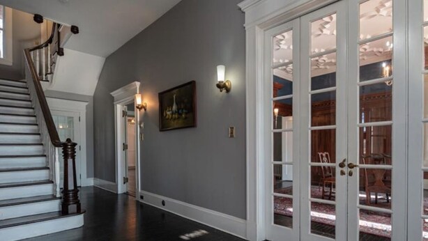 A hallway with dark wooden flooring, a staircase, and a set of glass doors leading to a dining area. - Spacious 6-bedroom house with AC, WiFi in charming Springfield (Springfield)