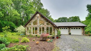 A stone cabin with a large glass window, surrounded by a well-maintained garden and a gravel driveway.