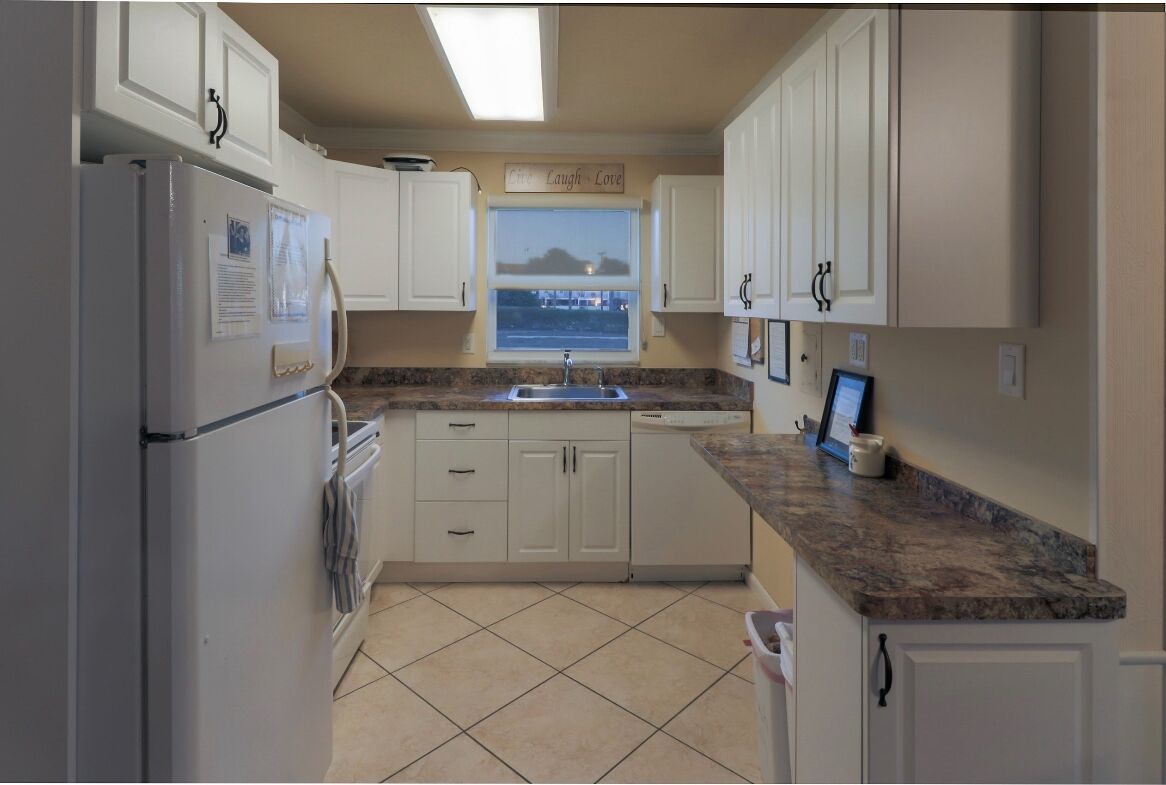 A kitchen with white cabinets, a granite countertop, a window with a view, and a refrigerator with papers on it.