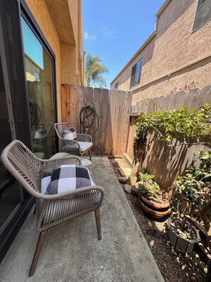 A patio area with wicker chairs, a checkered table, a wooden fence, and potted plants. - Modern Condo heart of North Park-2Bed-2ba-Parking-Laundry-AC (San Diego)