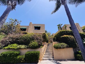 A staircase leading to a building with a beige facade, surrounded by lush greenery and palm trees. - Modern Condo heart of North Park-2Bed-2ba-Parking-Laundry-AC (San Diego)