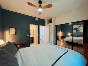 A bedroom with a large bed, a ceiling fan, a nightstand, a lamp, and a view of another room through a sliding door. - Modern Condo heart of North Park-2Bed-2ba-Parking-Laundry-AC (San Diego)