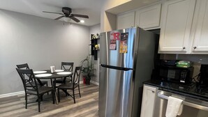 A modern kitchen with a stainless steel refrigerator, a microwave, and a dishwasher. There is a dining table with chairs and a ceiling fan.