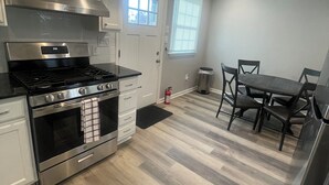 A modern kitchen with stainless steel appliances, a dining area with a table and chairs, and a window with blinds.