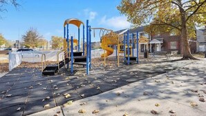 A playground with climbing structures and a slide, surrounded by trees and a white fence.