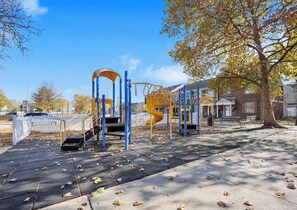 A playground with climbing structures and a slide, surrounded by trees and a white fence. - Riverside Retreat (Camden)
