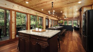 A spacious kitchen with a large island, wooden ceiling, and large windows offering views of the outdoors. - Soak Among the Treetops, Swim Indoors, Shoot Pool & Host Luxe Movie Nights - Whispering Pines Escape (Sevierville)