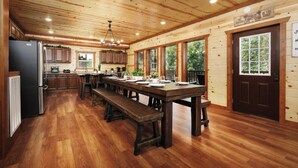 A spacious kitchen with wooden cabinets, a central island, and a dining area with benches. - Soak Among the Treetops, Swim Indoors, Shoot Pool & Host Luxe Movie Nights - Whispering Pines Escape (Sevierville)