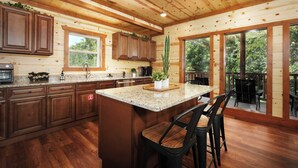 A spacious kitchen with wooden cabinets, a granite countertop, and a large island with bar stools. - Soak Among the Treetops, Swim Indoors, Shoot Pool & Host Luxe Movie Nights - Whispering Pines Escape (Sevierville)