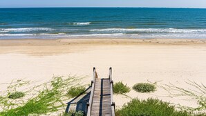 Ein hölzerner Steg führt zu einem Sandstrand mit Blick auf das Meer.