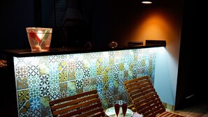 A dimly lit room with two wooden lounge chairs, a small table with two red glasses, and a tiled wall with a geometric pattern. - Big House Leisure 🌊 (Dourados)