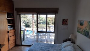 Ein Schlafzimmer mit einem Bett, einem Holzschrank, einer Schiebeglastür zu einem Außenbereich mit Pool und Gartenmöbeln.