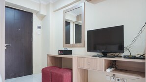 Ein Zimmer mit einem Holztisch, einem Fernseher, einem roten Hocker und einer Tür.