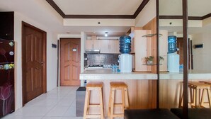 A modern kitchen with wooden cabinets, a countertop, and two stools. There are two large water dispensers on the counter.