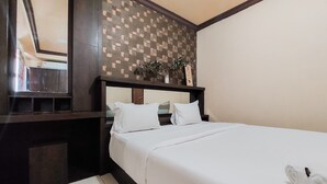 A hotel room with a large bed, a dark wooden headboard, a mirror, and a small plant on the headboard.